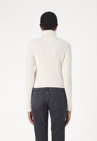 Maglione a collo alto a coste in tessuto bianco sporco, design aderente con maniche lunghe, abbinato a jeans grigio scuro con tasche posteriori.