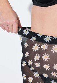 Collant neri trasparenti con un motivo a margherite bianche e gialle, dotati di una vita elastica e di una consistenza liscia. Tirando a mano l'area della vita.