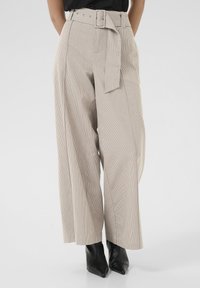 Pantaloni beige a righe, a vita alta, con cintura e design a gamba larga. La texture del tessuto appare liscia con una vestibilità strutturata.