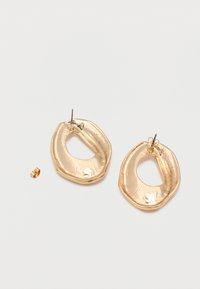 Ζευγάρι λαμπερά χρυσά σκουλαρίκια κρίκοι σε ακανόνιστο οβάλ σχήμα με ένα αποσυνδεδεμένο κλιπ πεταλούδας σε λευκό φόντο.