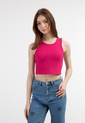 Roze geribbelde crop top met brede banden, gecombineerd met hoog getailleerde blauwe jeans met hartpatronen. Een eenvoudige zilveren ketting maakt de look compleet.