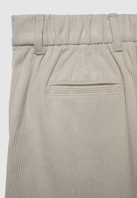 Beige Cordhosen mit einem breiten elastischen Bund, ausgestattet mit vertikalen Rippen und einer Gesäßtasche. Der Stoff hat eine weiche, strukturierte Oberfläche.
