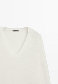 Maglione bianco a maglia con scollo a V, maniche lunghe, tessuto testurizzato e una piccola etichetta nera all'interno del collo.