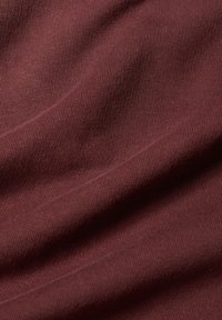 Primo piano di un morbido tessuto piegato di colore marrone rossiccio scuro che mostra la texture a maglia e leggere pieghe sotto una luce diffusa.