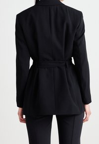 Sort skræddersyet blazer med indsnævret talje, spidse lapeller og lange ærmer. Glat stof med en struktureret design og subtile detaljer.