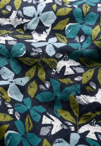 Materiał w kwiaty w odcieniach teal, białym i zielonym na ciemnogranatowym tle, o teksturowanym, tkanym wyglądzie.