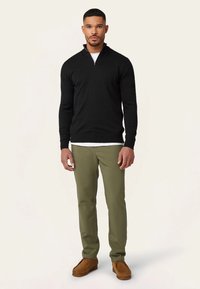 Zwarte trui met rits, olijfgroene broek en bruine mocassinschoenen. Gladde textuur, aansluitend ontwerp en neutrale kleuren.