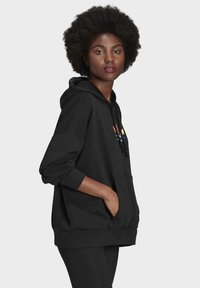 Felpa nera con cappuccio e cordino, tasche laterali e accenti di logo colorati in arancione, giallo e blu sul petto. Tessuto morbido e con una texture.