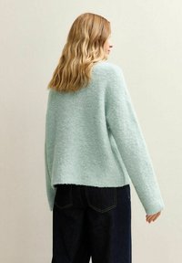 Ljus mintgrön stickad tröja med en texturerad finish, rund halsringning och nedsläppta axlar, i kombination med mörka denimjeans.