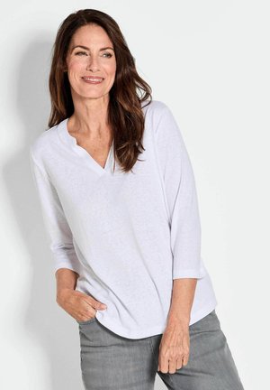 Witte top met driekwartmouwen en een V-hals, gemaakt van lichtgewicht stof, gecombineerd met grijze jeans. Glad textuur, relaxed fit.