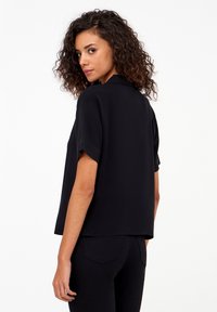 Top nero a maniche corte con vestibilità ampia, orlo dritto e colletto sottile. Materiale leggero con una texture liscia.