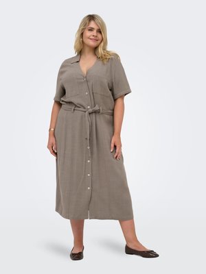 Kvinde iført en midi-kjole i taupe med knapper foran, korte ærmer og bånd i taljen, kombineret med brune ballerinasko, stående mod en hvid baggrund.