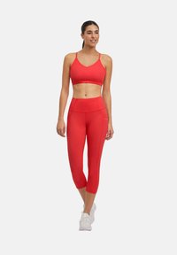 Completo attivo rosso composto da un reggiseno sportivo con scollatura a V e leggings a vita alta. Realizzato in tessuto elastico e liscio con cuciture sagomate.