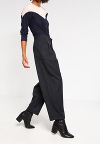 Svarta vida byxor med hög midja, kombinerat med en långärmad topp i marinblått och beige färgblock och svarta klackiga ankelstövlar.