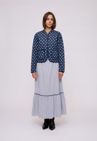 Giacca trapuntata blu navy con motivo a diamante bianco, maniche lunghe e due tasche frontali. Abbinata a una gonna lunga a righe e stivali neri.
