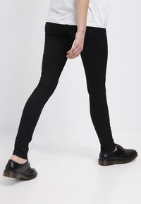 Jeans negros ajustados de tejido elástico, con una textura suave y un corte slim. Combinados con zapatos negros con cordones.
