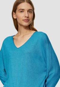 Turkusowy sweter dzianinowy z dekoltem w serek, luźnymi rękawami i teksturowanym wykończeniem, wykonany z miękkiego, lekkiego materiału. Prosty i nowoczesny design.