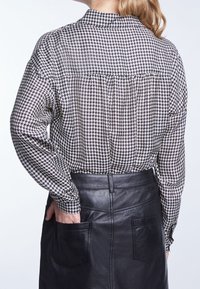 Chemise à manches longues au motif pied-de-poule noir et blanc, avec col et plis, associée à une jupe en cuir noir élégante avec poches.