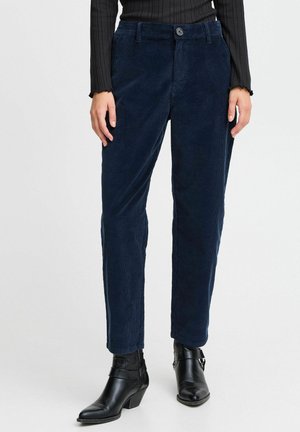 Pantaloni in velluto a coste blu navy con taglio dritto, dotati di chiusura con bottone, tasche laterali e una texture morbida, abbinati a stivaletti neri alla caviglia.