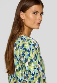 Bunt gemusterte Bluse in verschiedenen Grüntönen, Blau und Beige. Leichter Stoff mit rundem Ausschnitt und langen Ärmeln.