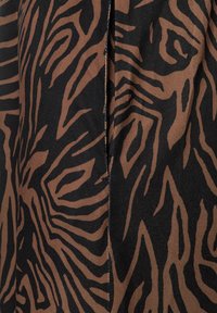 Stoff mit schwarzem Grund und einem braunen Tigerstreifenmuster. Glatte Textur mit einer leicht glänzenden Oberfläche und sichtbaren Nahtdetails.