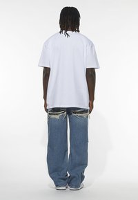 Fehér, túlméretezett rövid ujjú póló, laza szabású kék farmernadrággal, amely kopott részletekkel és rojtos széllel rendelkezik.