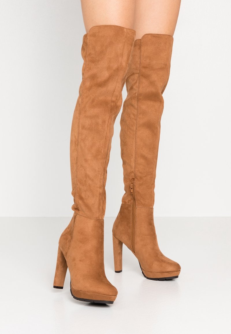 Botki do kolan w kolorze jasnobrązowym z zamszu, z grubym wysokim obcasem, zamkiem błyskawicznym z boku oraz platformą, o gładkiej teksturze i dopasowanym kroju.