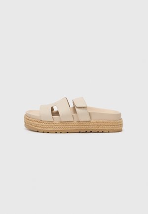 Beige platformsandal med brede stropper og fletmed jutesål på en neutral baggrund.