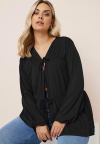Blusa nera con scollo a V, laccio in vita, maniche lunghe e vestibilità rilassata. Tessuto liscio e leggero con una sottile trama.