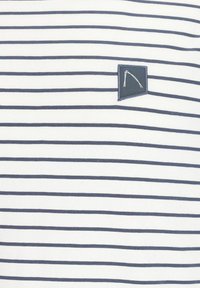 Balta, medvilninė T-shirt marškinėliai trumpomis rankovėmis, dekoruoti tamsiai mėlynomis horizontaliomis juostelėmis ir mažąja tamsiai mėlyna logotipo etikete kairėje pusėje.