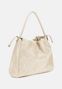 Borsa a mano beige trapuntata con una superficie morbida e texture, un'apertura ampia e un'unica maniglia liscia. Presenta dettagli di cucitura sottili.