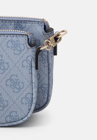 Double poche en tissu bleu avec fermeture éclair et fermoir dorés, présentant un motif floral tissé subtil et une bordure noire sur fond blanc.