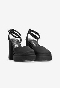 Tacones de plataforma negros hechos de un tejido suave, con un ancho tacón cuadrado y correas para los tobillos. Punta redondeada y plantilla acolchada para mayor comodidad.