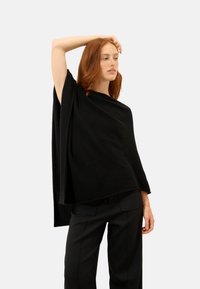 Czarny dzianinowy ponczo o luźnym kroju, okrągłym dekolcie i zwisających rękawach, w połączeniu z dopasowanymi czarnymi spodniami. Gładka faktura.