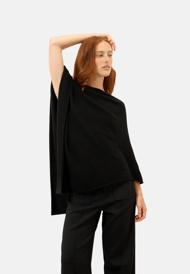 Czarny dzianinowy ponczo o luźnym kroju, okrągłym dekolcie i zwisających rękawach, w połączeniu z dopasowanymi czarnymi spodniami. Gładka faktura.