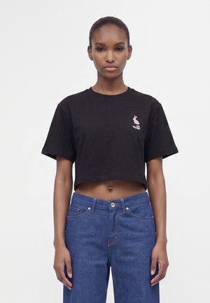 Γυναίκα που φοράει μαύρο cropped T-shirt με μικρό ροζ κουνελάκι και κείμενο "LOVE Moschino", συνδυασμένο με ψηλόμεσο μπλε τζιν.