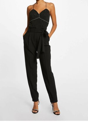 Zwarte jumpsuit met een getailleerde bovenkant voorzien van sprankelende details, dunne bandjes, en wijduitlopende broeken met een strik taille. Zwarte sandalen met bandjes.