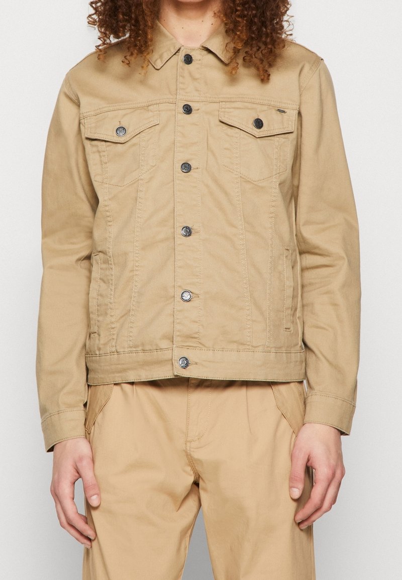 Khaki dżinsowa kurtka z klasycznym kołnierzem, zapięciem na guziki i dwoma kieszeniami na piersi. Posiada długie rękawy i prosty krój.