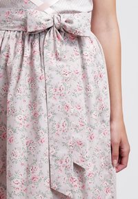 Main d'une femme reposant à côté d'une jupe gris clair avec un motif floral rose et un grand nœud en tissu noué à la taille.