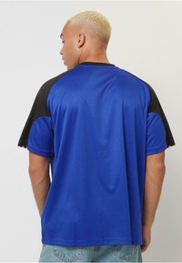 Blå och svart kortärmad tränings T-shirt med en enfärgad blå kropp, svarta raglanärmar och ett mjukt, lätt tyg.