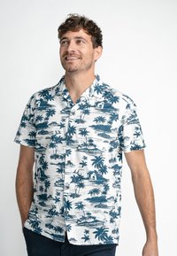 Chemise à manches courtes avec des boutons, blanche, ornée d'un imprimé tropical bleu représentant des palmiers, des bateaux et des scènes d'île. Tissu texturé.