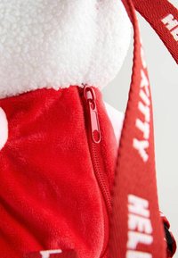 Röd plyschryggsäck med ett mjukt vitt fleecelock. Den har en röd dragkedja och ett rem med texten "HELLO KITTY" i vitt.