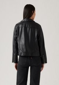 Zwarte leren jack met een klassieke kraag, cropped ontwerp en zichtbare stiksels. Ritsmanchetten en een gladde textuur, van achteren getoond.