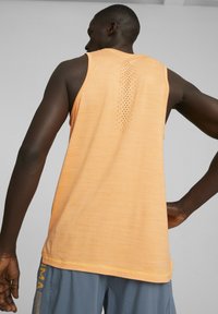 Débardeur de sport sans manches orange avec un tissu texturé et un dos perforé pour la ventilation, assorti à un short gris.