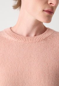 Pull en tricot rose clair avec un col rond côtelé, présentant une texture douce et une finition lisse.