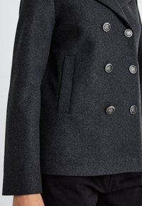 Blazer grigio in misto lana con doppiopetto, caratterizzato da sei bottoni metallici, colletto a punta e tasca laterale con finitura testurizzata.
