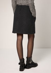 Grijze wollen rok met een rechte snit, twee achterzakken en een naaddetail, gecombineerd met zwarte enkellaarsjes en doorschijnende panty's.