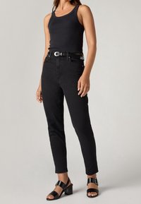 Débardeur noir associé à un jean noir taille haute et des sandales noires à talons blocs ; texture lisse, coupe ajustée, détails accentués minimalistes.