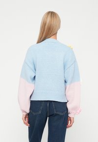 Ανοιχτό μπλε πλεκτό πουλόβερ με ροζ λεπτομέρειες, φαρδιά μανίκια, ριμπ τελείωμα και υφασμάτινες πλέξιμο λεπτομέρειες σε μπαλάκια στους ώμους.