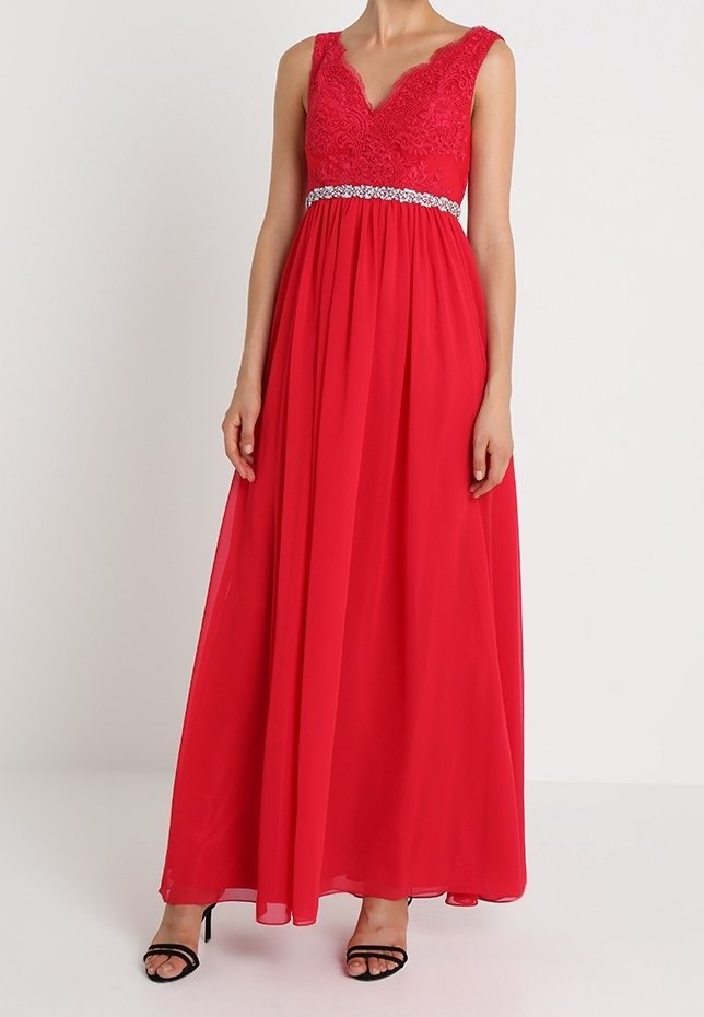 Robe de soirée rouge sans manches avec corsage en dentelle, ceinture à la taille ornée de strass, jupe fluide en chiffon, portée avec des sandales noires à talons hauts et à lanières.